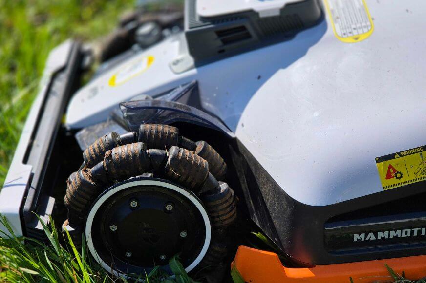 Ein Mähroboter mit OMNI-direktionalen Rändern steht auf dem Rasen und man sieht in der Nahaufnahme das Profil